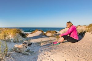 6 ultimative Gründe für die Völklinger Hütte Frau sitzt am Strand und schaut Ihren Hund an. Sie sitzen in den Dünen und hinter ihnen ist die Strandkulisse von der Halbinsel Peniche in Portugal